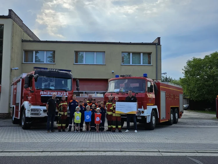 Daniel Ziegler, Technischer Geschäftsführer von EEW Großräschen (re.), und Produktionsleiter Marcus Rostalski (li.) sagen Danke und übergeben Gina Zukunft, Betreuerin der Jugendfeuerwehr (2. v.l.), Olaf Schulz, Kinderfeuerwehrwart (M.), Robin Metzger, Jugendfeuerwehrwart (3. v.r.), Robert Noack, Ortswehrführer (2. v.r.), sowie der Kinder- und Jugendfeuerwehr der Ortswehr Großräschen-Nord (mittig) einen symbolischen Spendenscheck über 1.000 Euro.